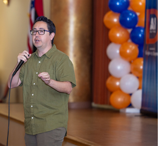A speaker addressing the AI in the D audience beside orange and blue balloon decor