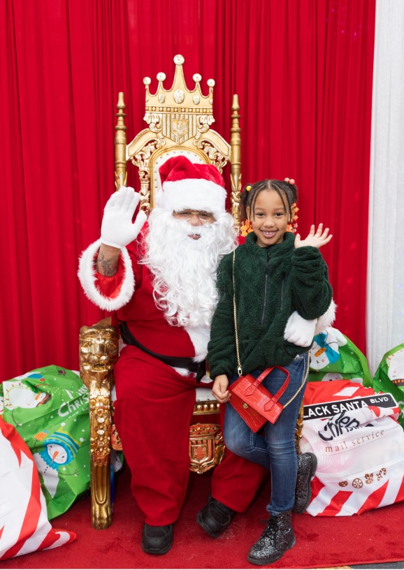 A girl in a green fleece waving beside Santa on his gold throne