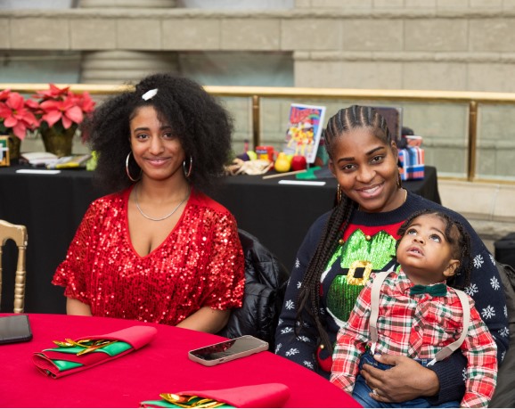 Two women and a toddler smiling at a red-draped table