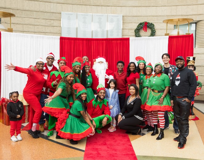 Elves and guests posing with Santa in front of the red and white backdrop