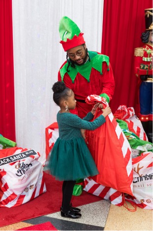 A little girl receiving a gift bag from an elf